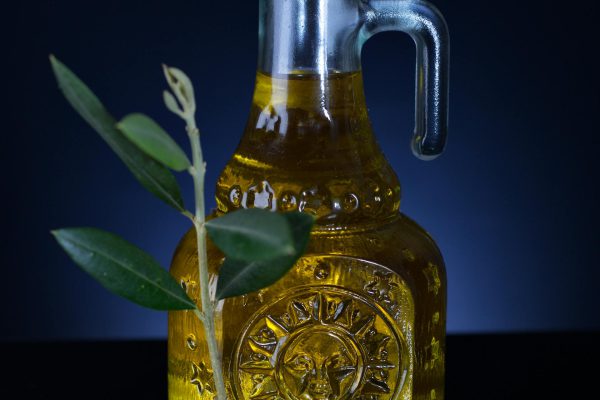 Tamsaus stiklo alyvuogių aliejaus butelis ir šviežios žalios alyvuogės ant medinio paviršiaus.