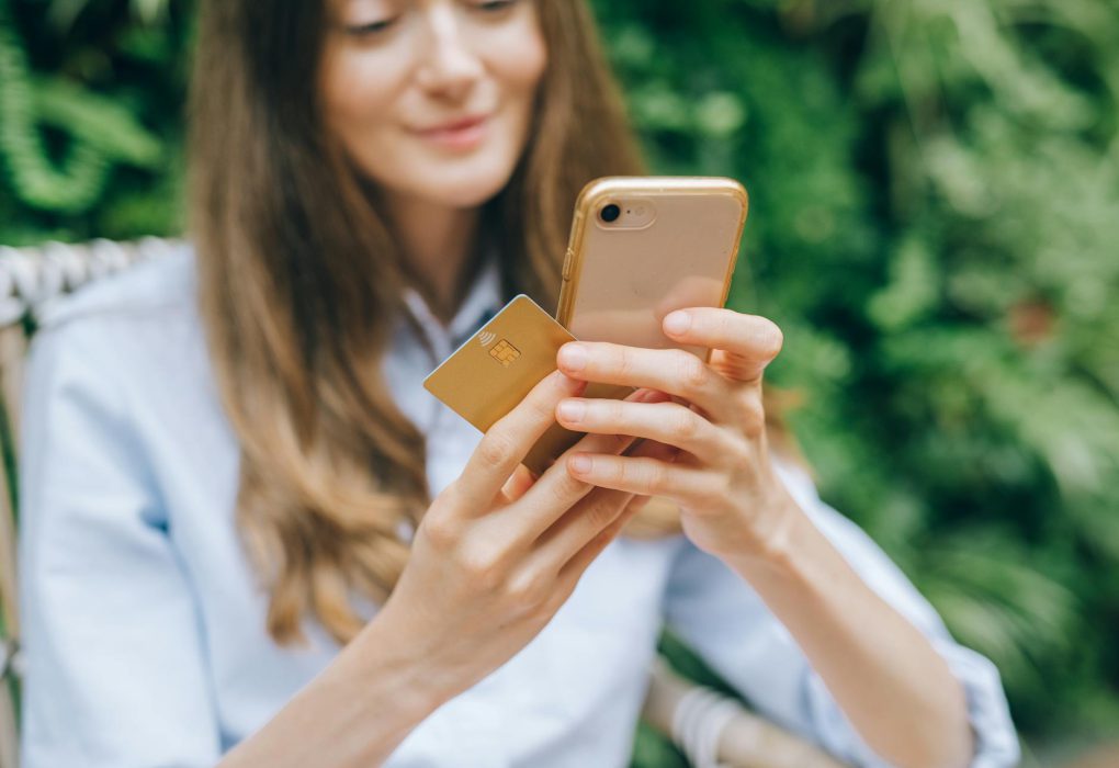 Moteris telefone peržiūri buities prekių nuolaidų leidinį šviesiame namų interjere.
